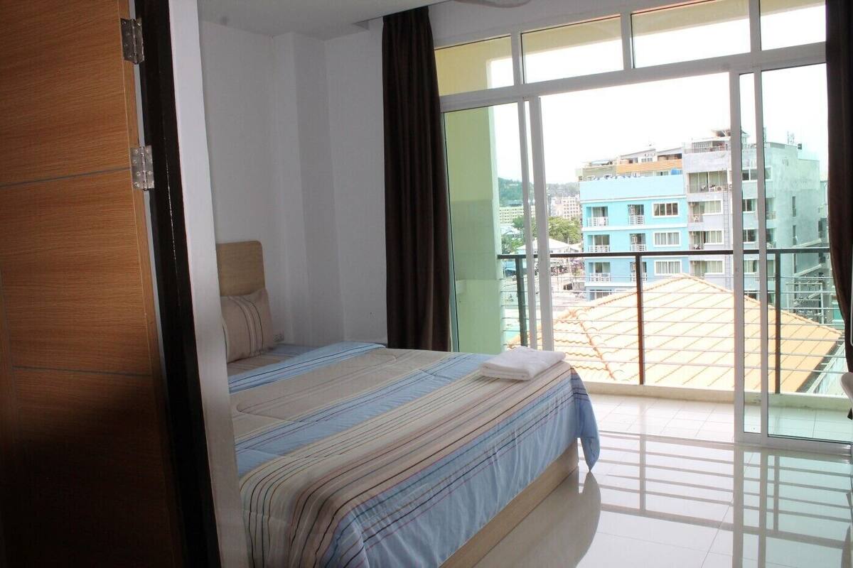 Un dormitorio con cama, ventana y vista a edificios.