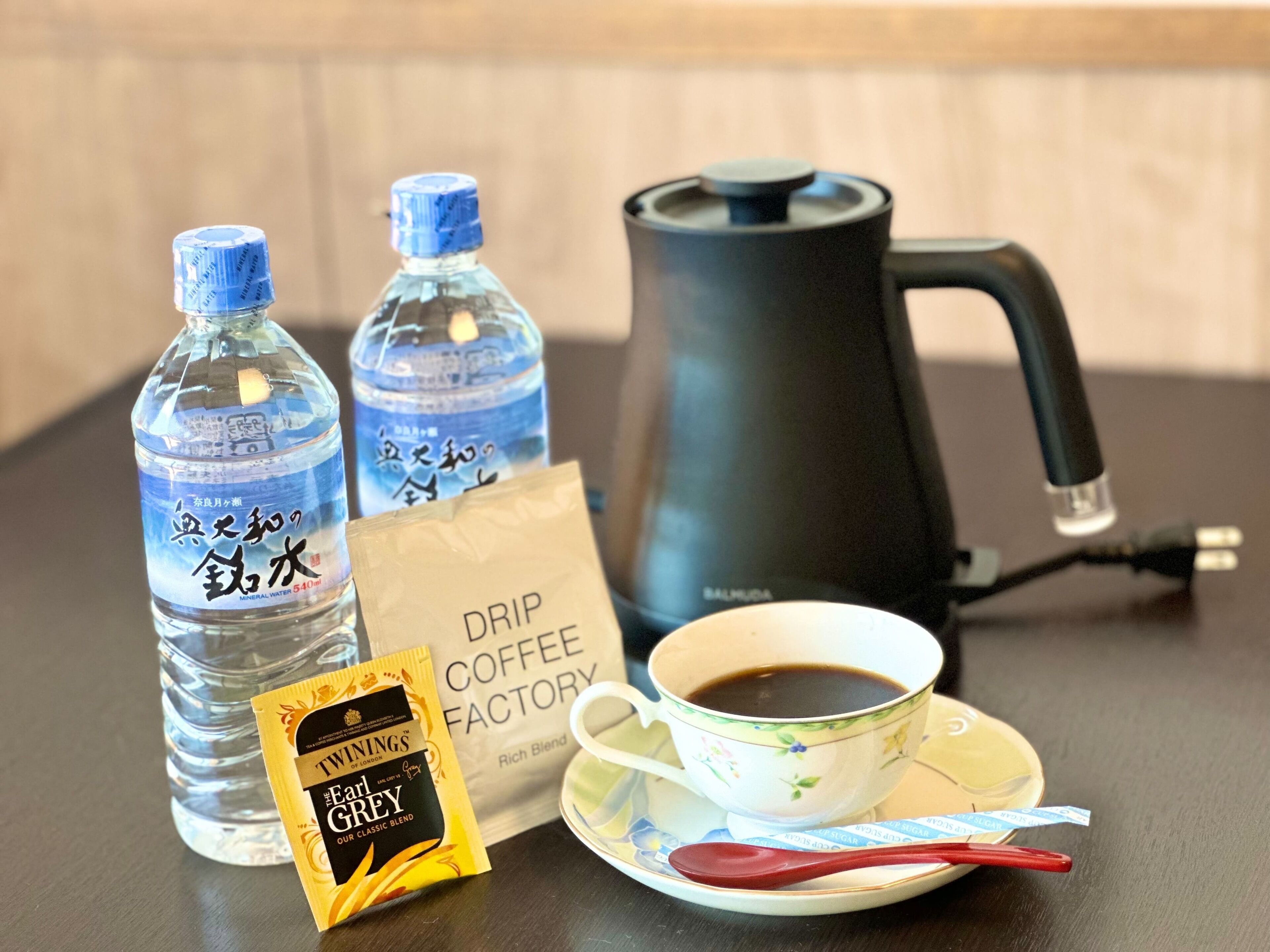 A table with mineral water bottles, a drip coffee bag, a coffee maker, and a cup of coffee.