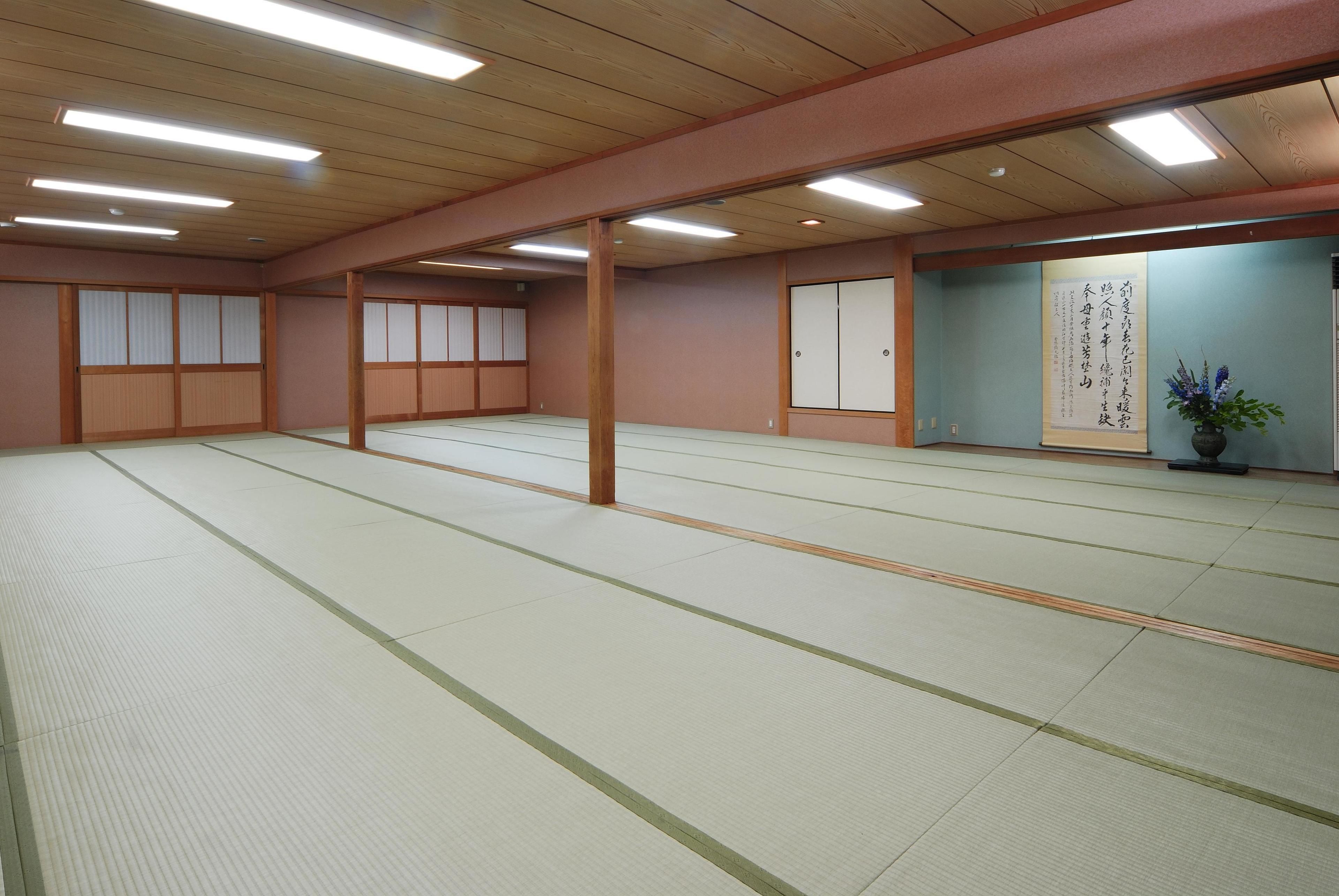 A traditional Japanese room with tatami flooring, wooden beams, sliding doors, and a large calligraphy scroll on the wall.