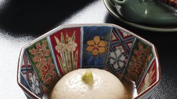 A bowl of white rice with a green garnish, a plate with a piece of meat and vegetables, and a green teapot on a black table.