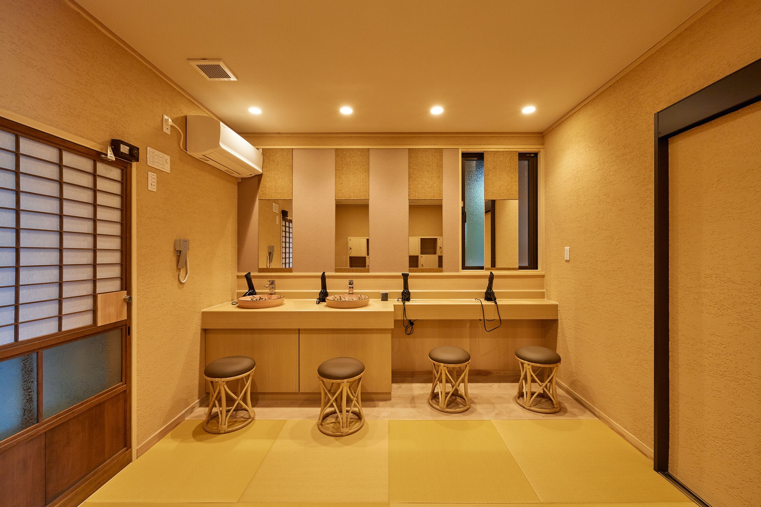 A hotel bathroom with a sink, mirror, and three stools.