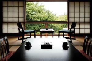 A traditional Japanese room with tatami flooring, a low table, two chairs, and a view of greenery through a shoji screen.