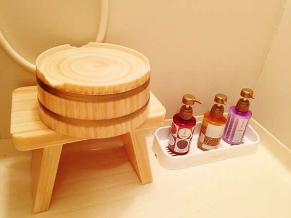A wooden stool with a round seat and a matching lid, placed on a white surface next to a tray holding four bottles of shampoo. - Yoshinoso Yukawaya (Yoshino)