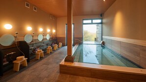 Un spa moderno con una amplia piscina interior, bancos de madera y varios espejos.