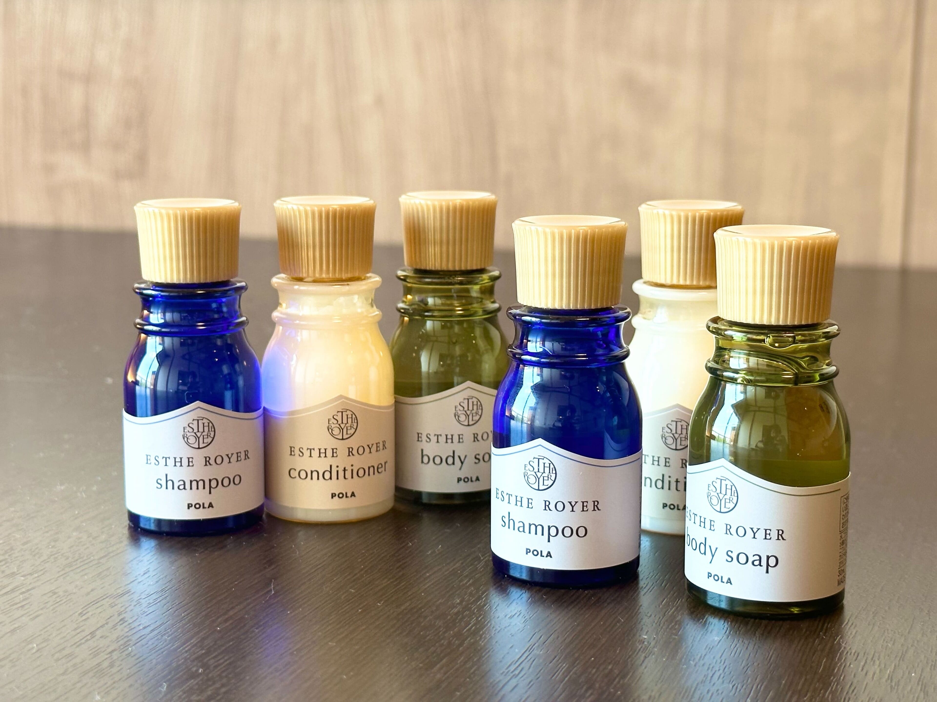 Six small bottles of ESTHE ROYER body products on a wooden surface.
