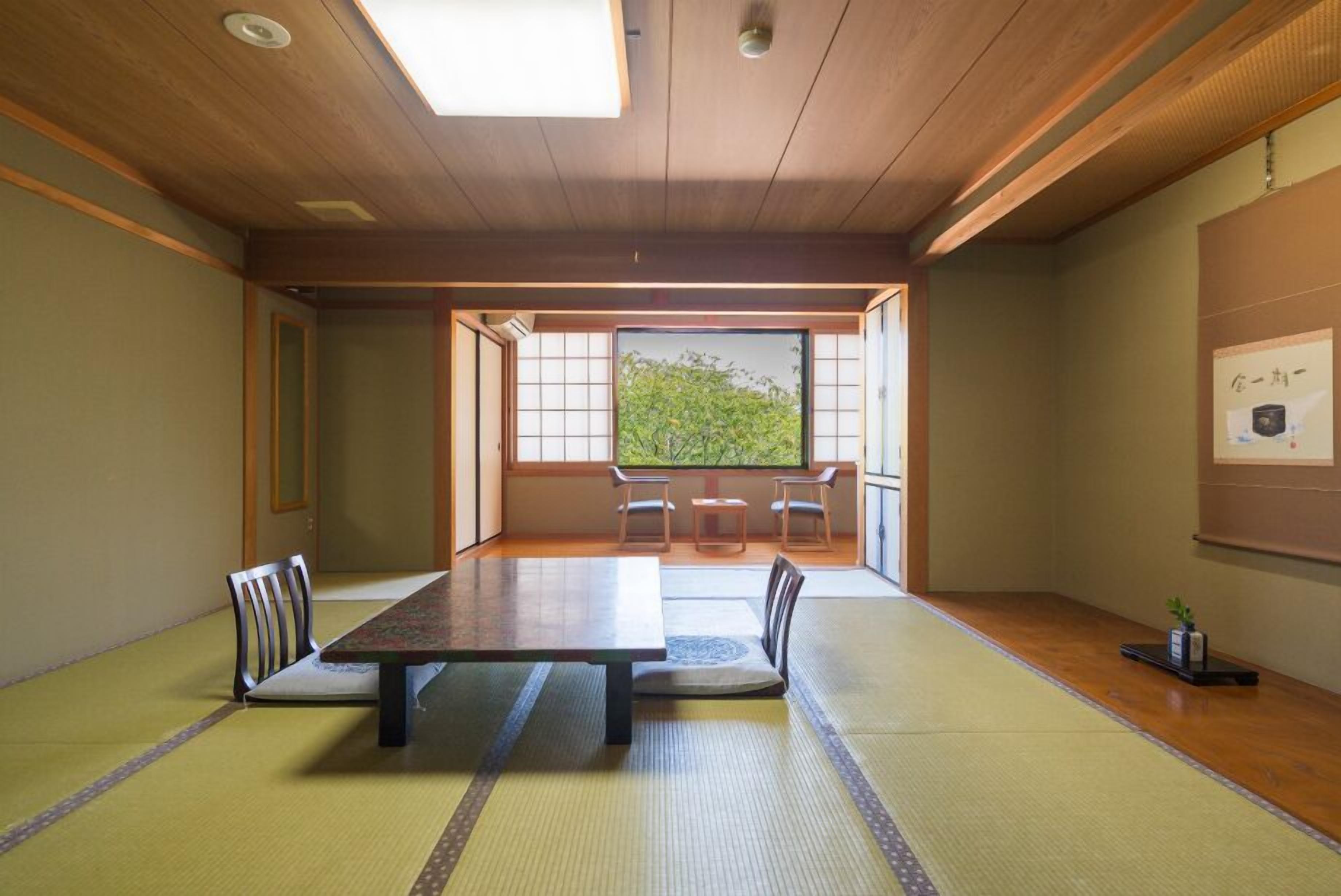 Une pièce avec un sol recouvert de tatamis, une table en bois, des chaises et une vue à travers un paravent en papier de riz (shoji).