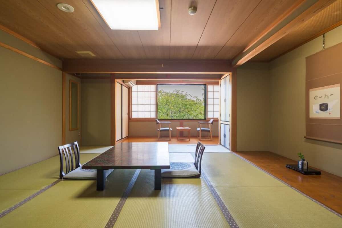 Una habitación con esterillas de tatami, una mesa de madera, sillas y vistas a través de un panel shoji.