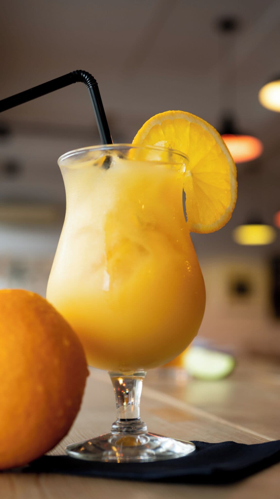 Um copo de sumo de laranja com canudo preto e uma fatia de laranja como guarnição sobre uma mesa.