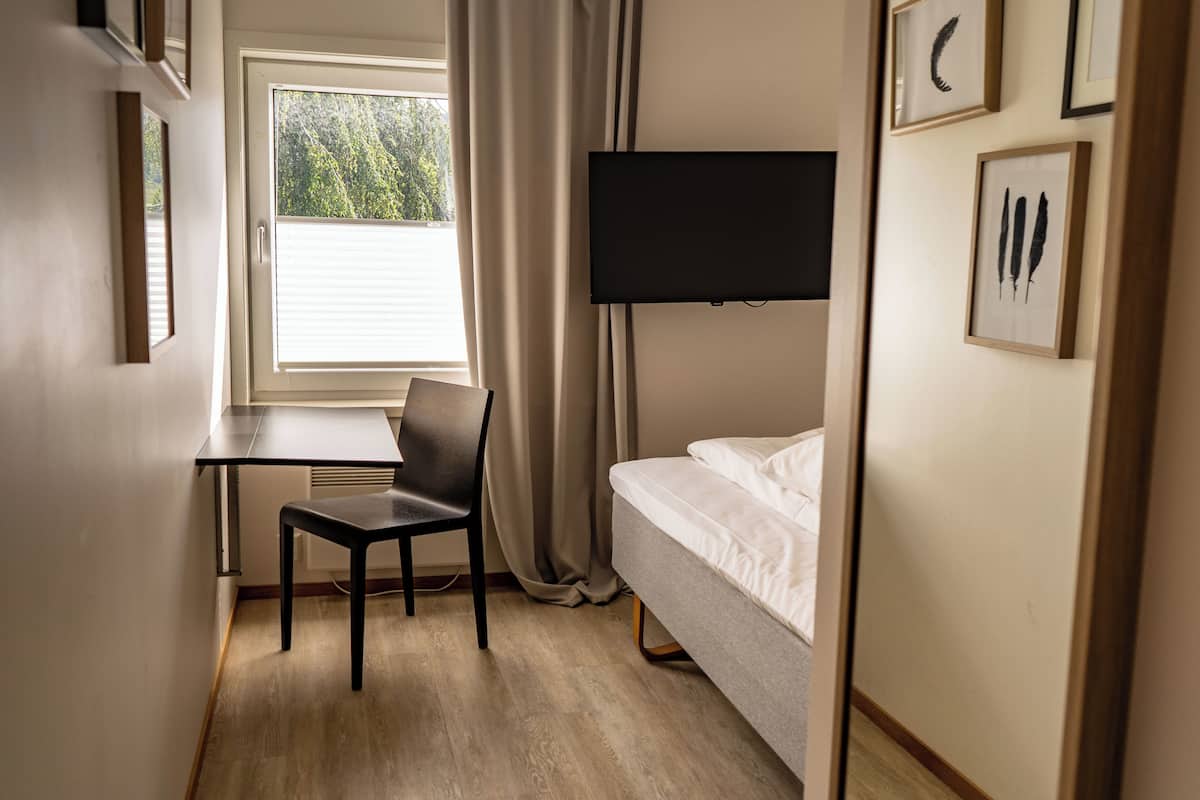 Habitación de hotel con cama, escritorio, silla, televisor y ventana con cortinas.
