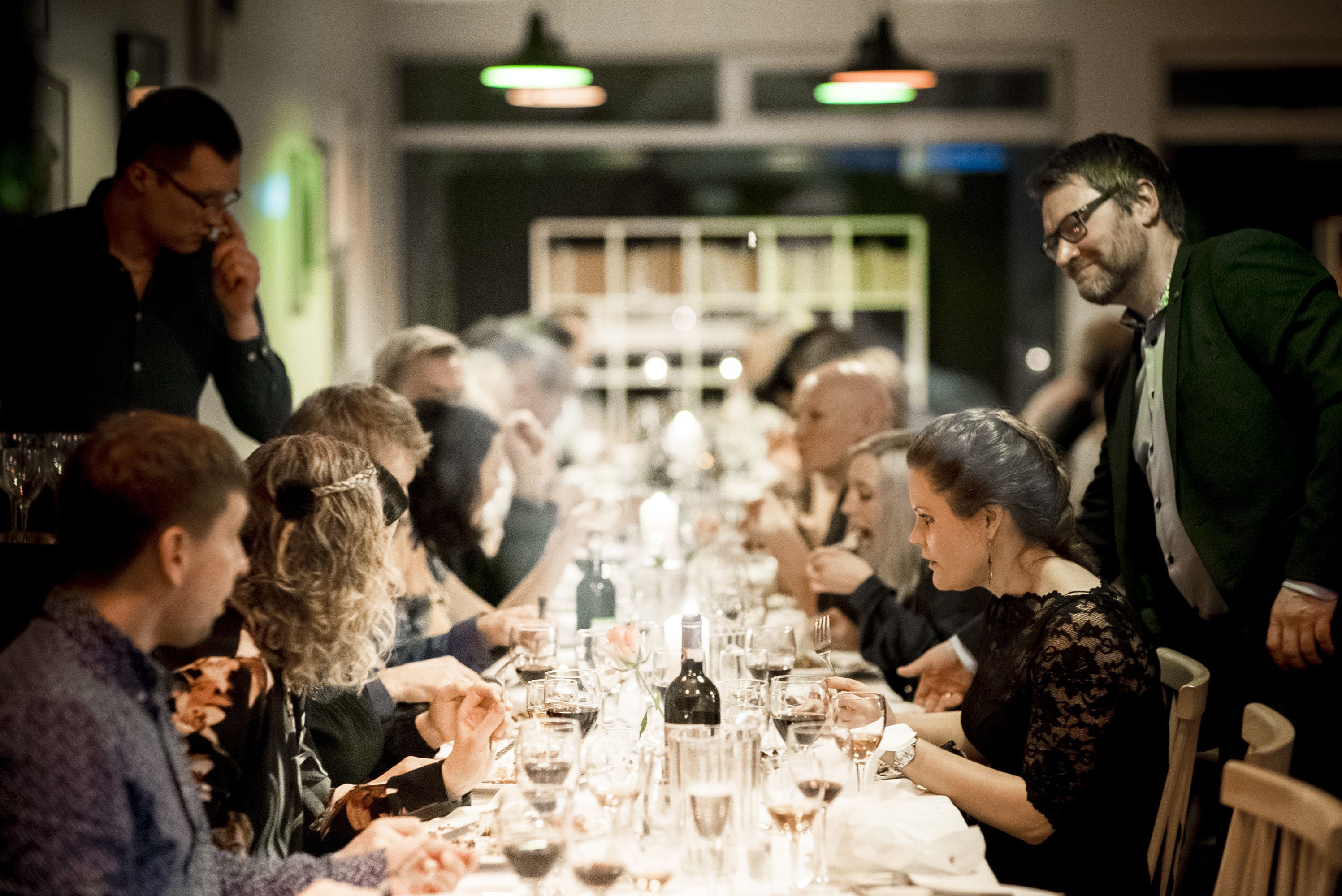 Una larga mesa de comedor con varias personas sentadas, rodeada de copas y botellas de vino.
