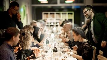 Una larga mesa de comedor con varias personas sentadas, rodeada de copas y botellas de vino.