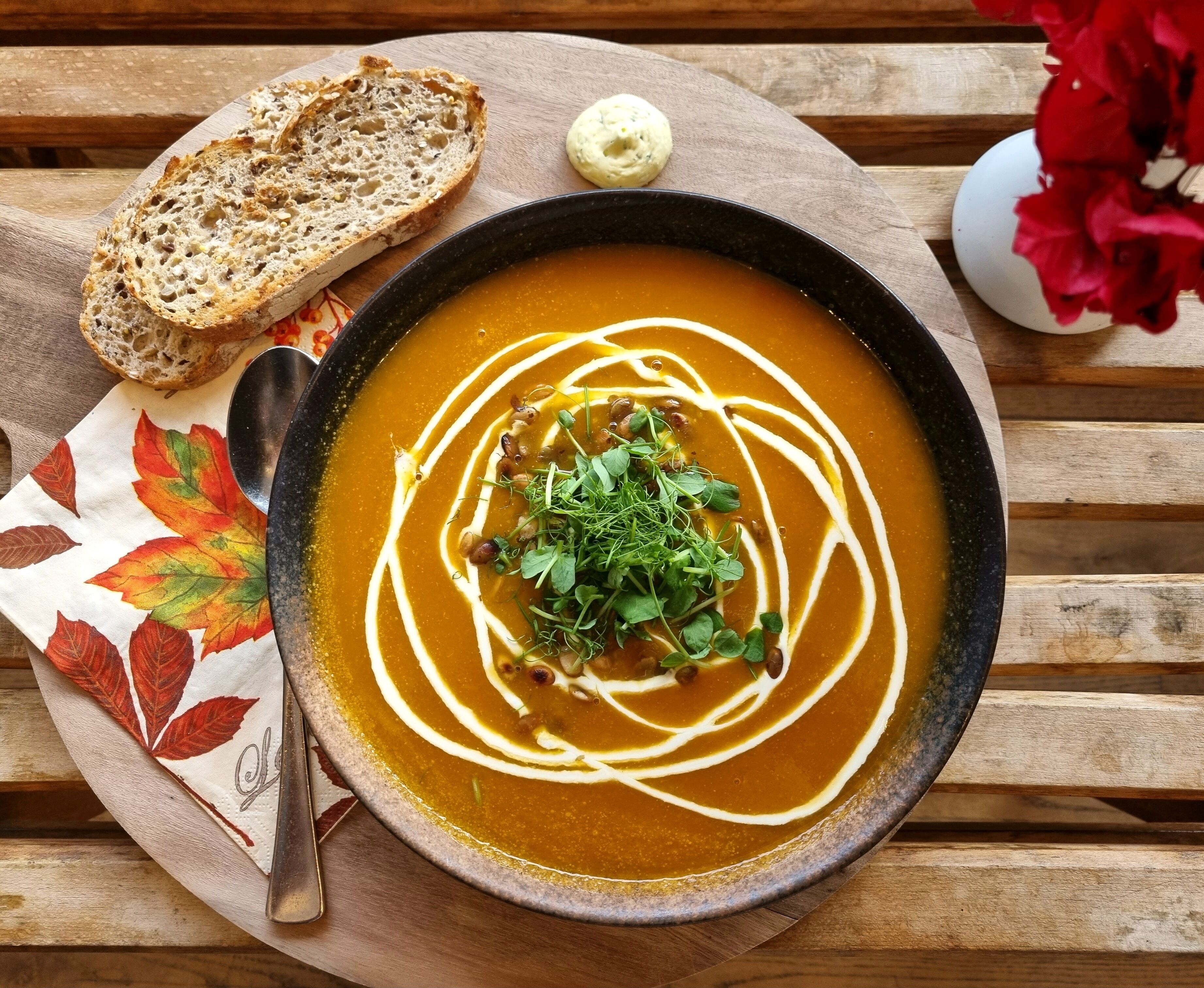 A bowl of soup with a garnish, a spoon, and a piece of bread on a wooden table.