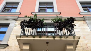 A building facade with a stone entrance, a black metal balcony with plants, and a hanging chandelier. - Rudolfo  Hotel (Lviv)