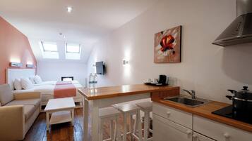 Un espacio habitable compacto con kitchenette, un sofá, una mesa de centro y un cuadro en la pared.