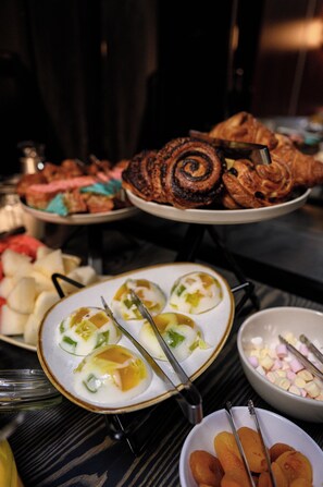 A buffet with various dishes including pastries, fruits, and a bowl of marshmallows.