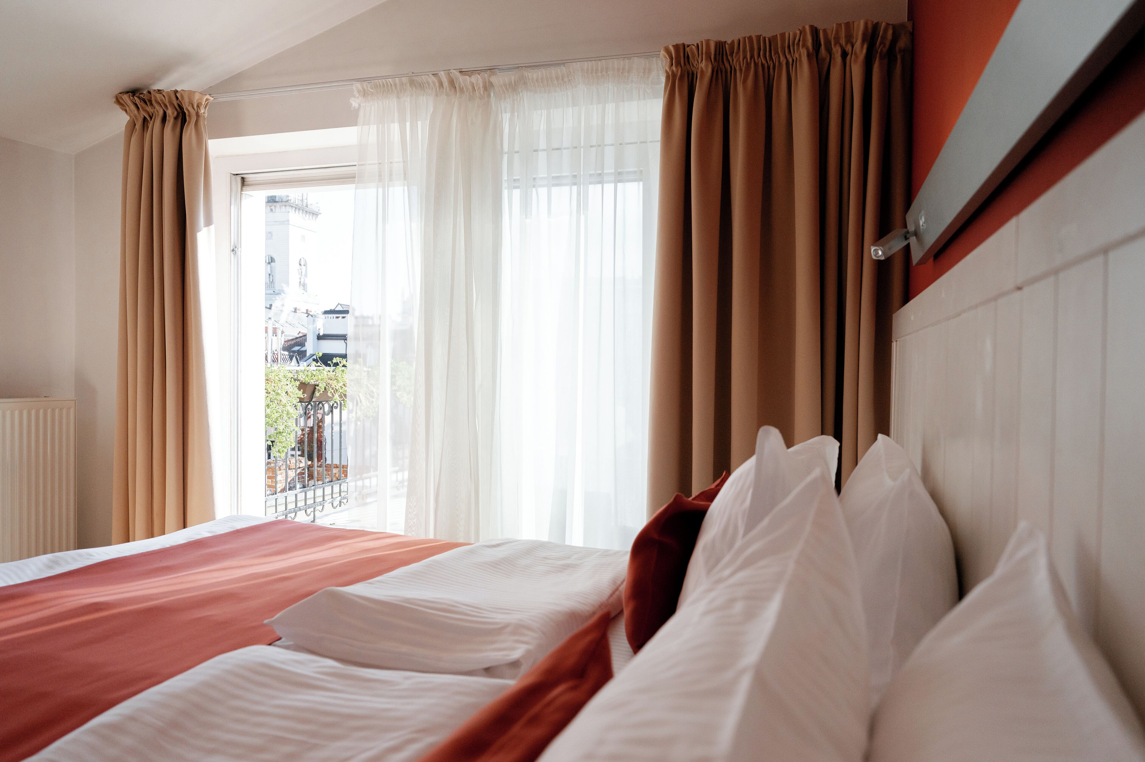 Habitación de hotel con una cama grande, cortinas color beige y vistas al exterior.