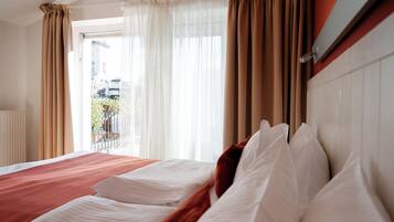 Habitación de hotel con una cama grande, cortinas color beige y vistas al exterior.