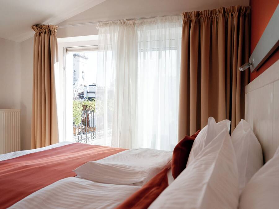 Habitación de hotel con una cama grande, cortinas color beige y vistas al exterior.
