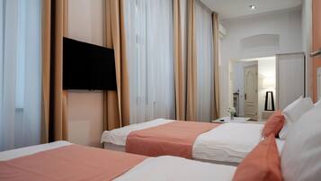 A hotel room with two beds, beige curtains, a flat-screen TV mounted on the wall, and a door leading to a bathroom.