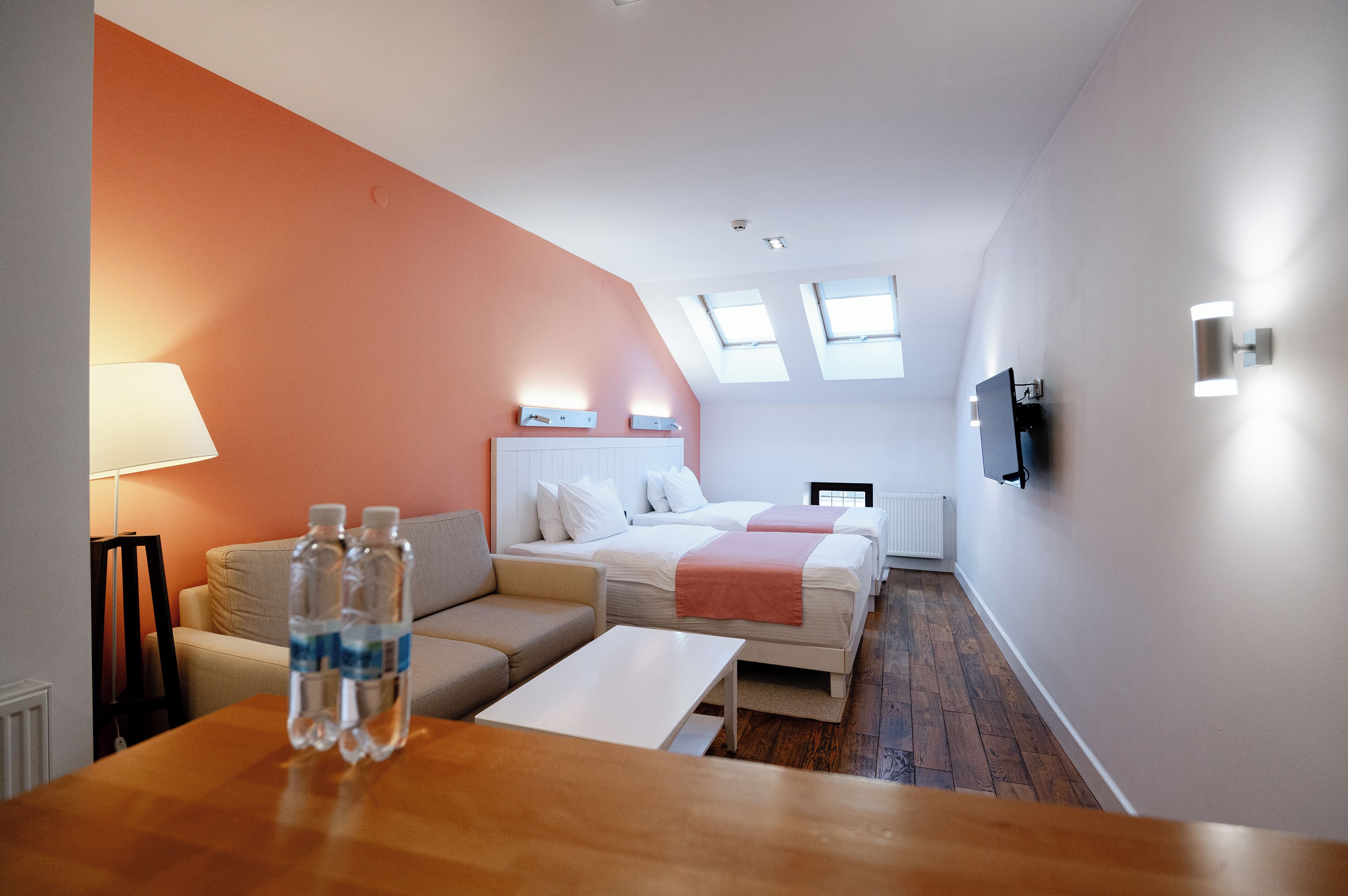 Ein Hotelzimmer mit einer Couch, zwei Betten, einem Fernseher und einem Tisch mit Wasserflaschen.
