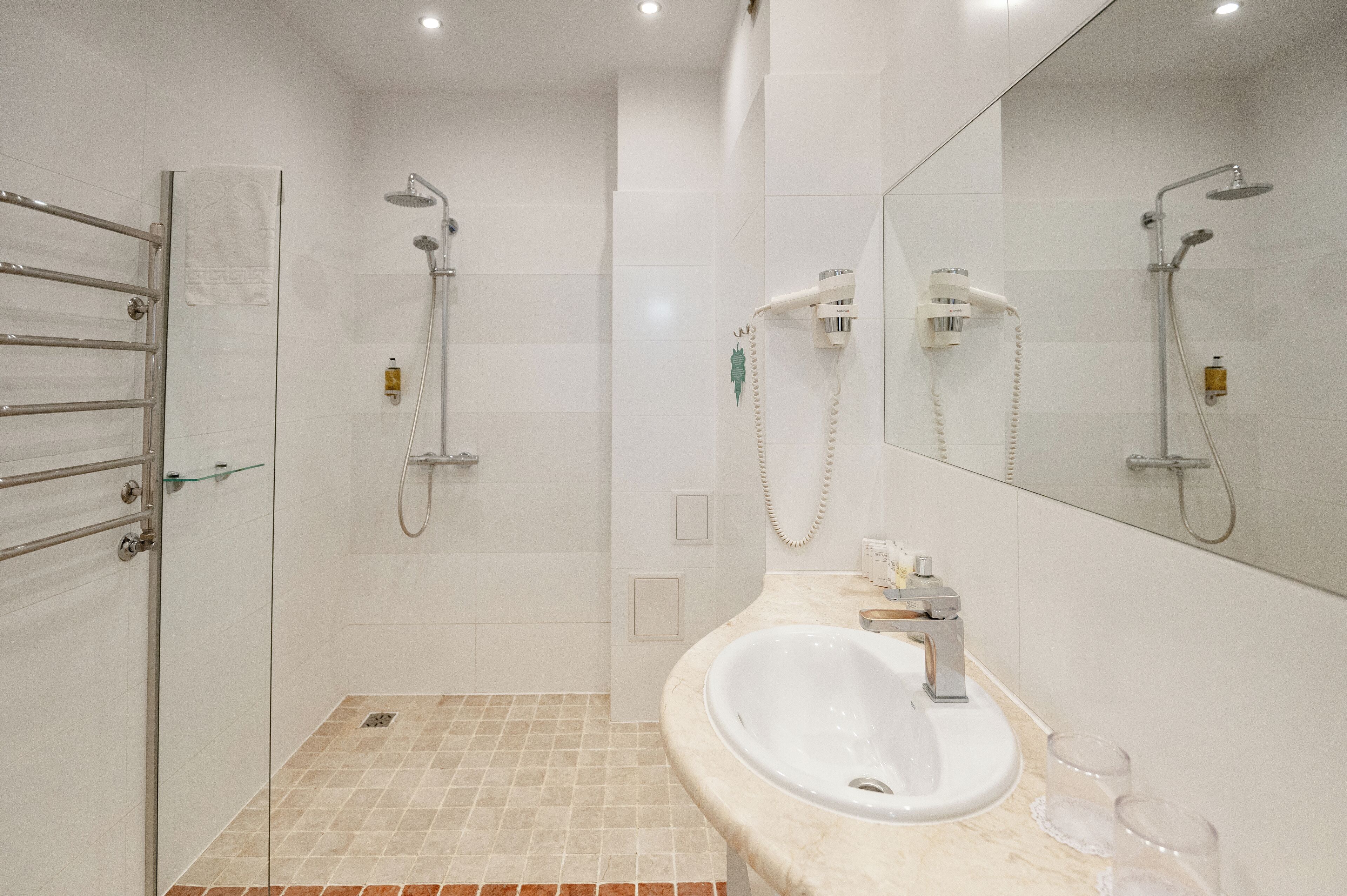 Ein modernes Badezimmer mit Duschkabine aus Glas, einem weißen Waschbecken mit Spiegel und einem Handtuchhalter.