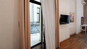 A modern living room with a flat-screen TV mounted on the wall, a radiator, and a window with beige curtains. - Rudolfo  Hotel (Lviv)