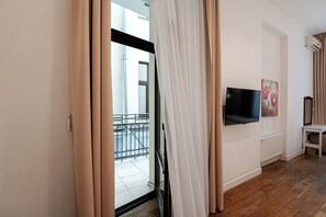A modern living room with a flat-screen TV mounted on the wall, a radiator, and a window with beige curtains.