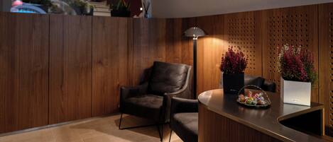 A modern reception area with a wooden wall, a leather chair, a desk with a basket of snacks, and a potted plant.