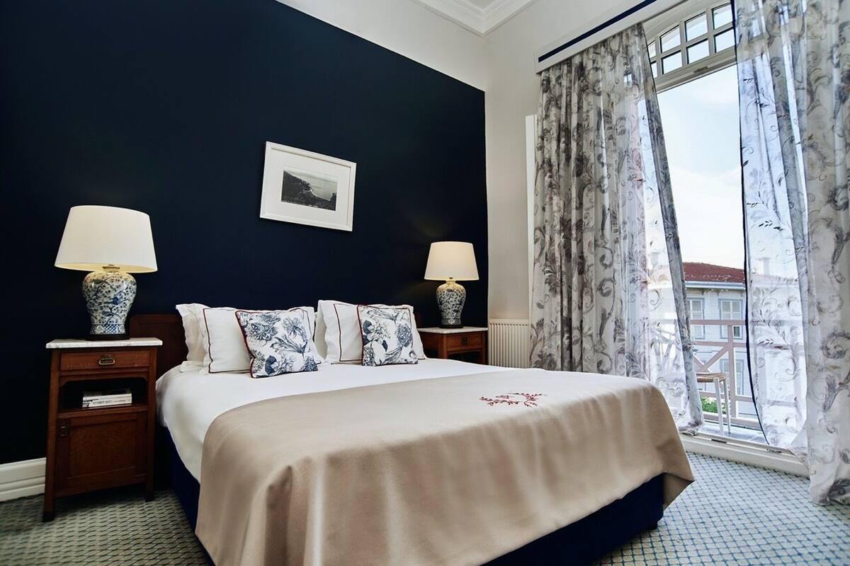Une chambre d’hôtel avec un grand lit, deux tables de chevet avec des lampes, un tableau encadré au mur et une fenêtre avec des rideaux.