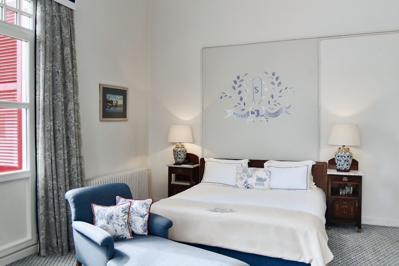 A hotel room with a bed, two bedside tables with lamps, a window with curtains, a framed picture on the wall, and a decorative wall piece.