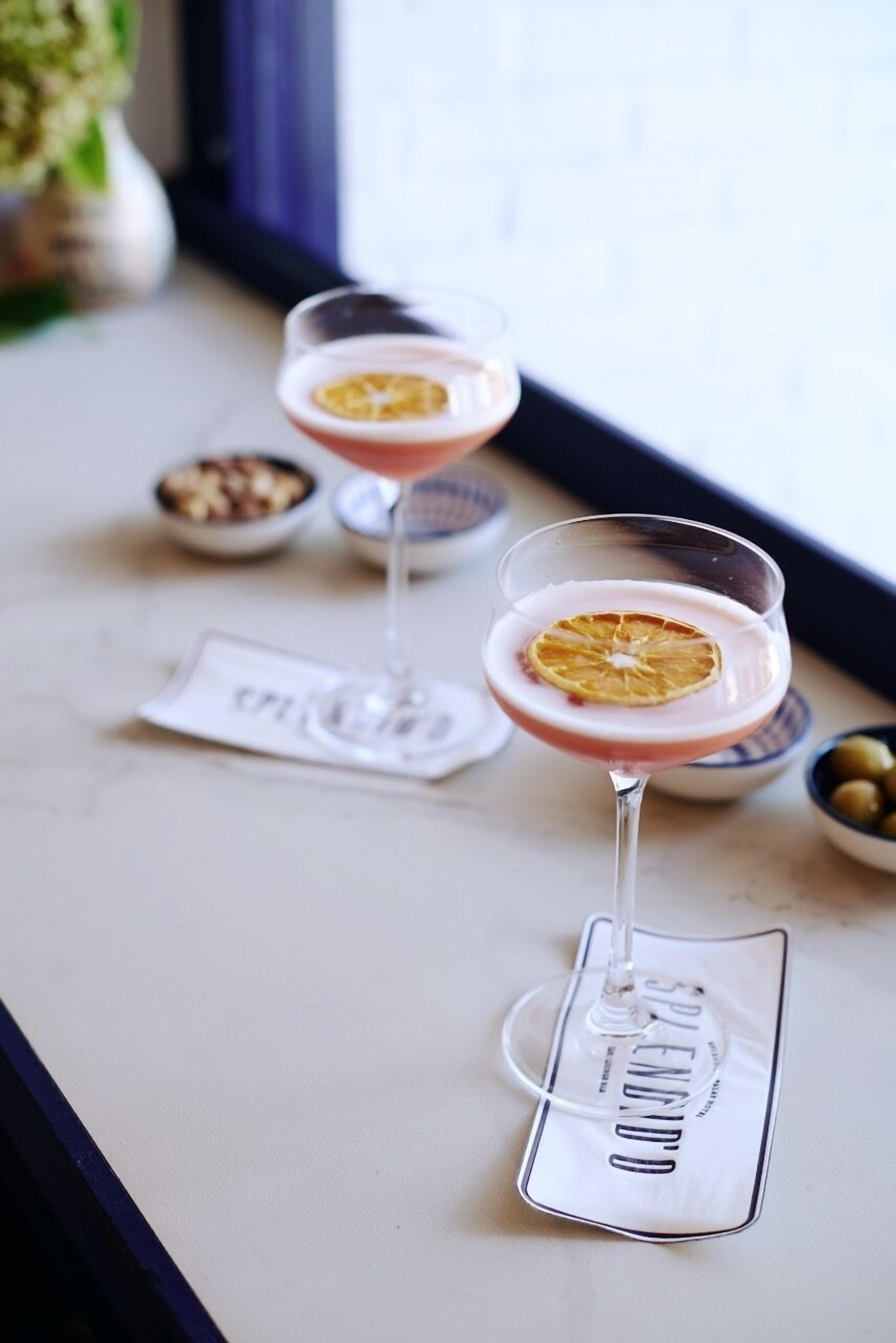 Three martini glasses with a pink drink and a dried orange slice on a table near a window.