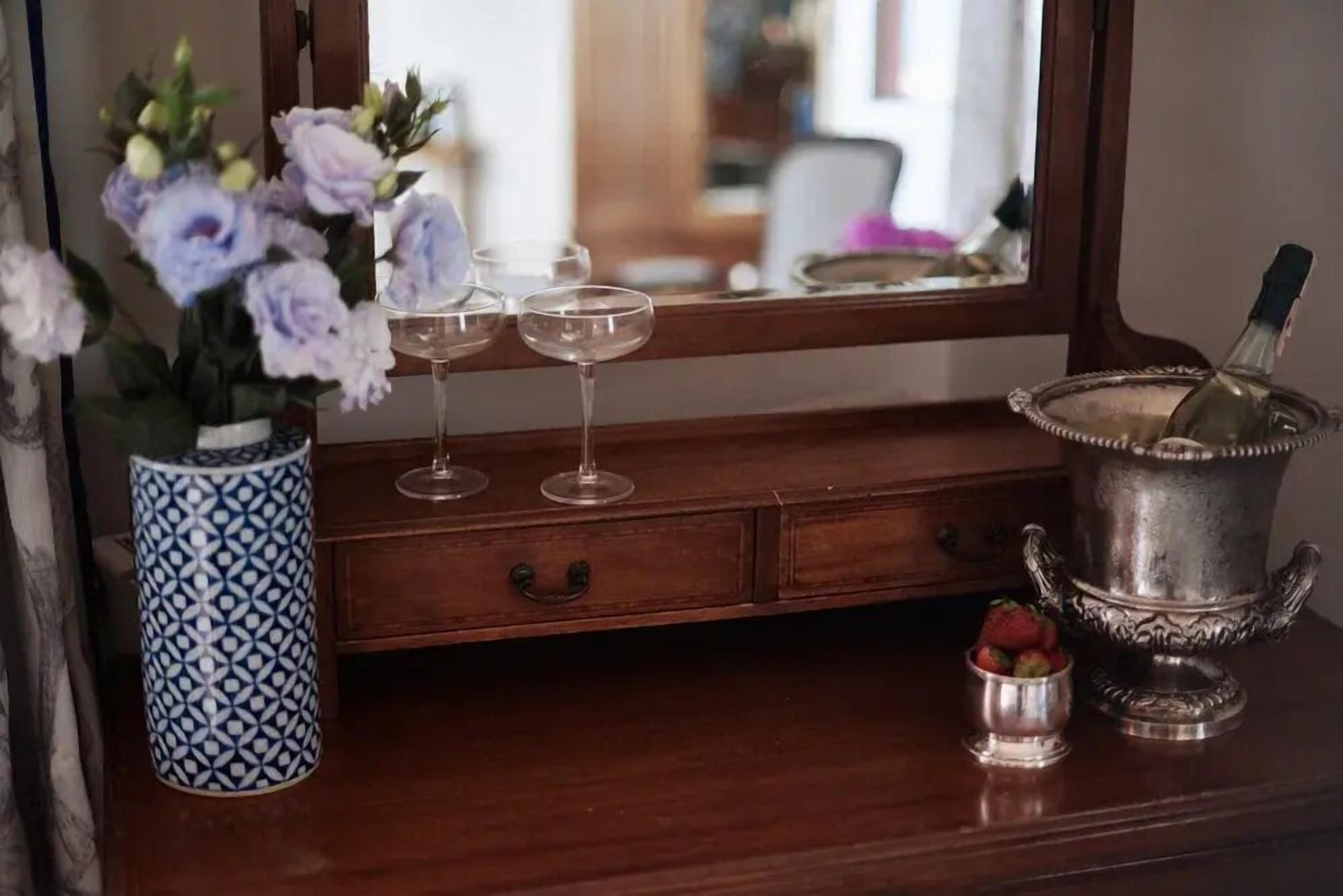 En byrå i trä med en vas med blommor, två vinglas, en silverhink och en liten skål med jordgubbar.