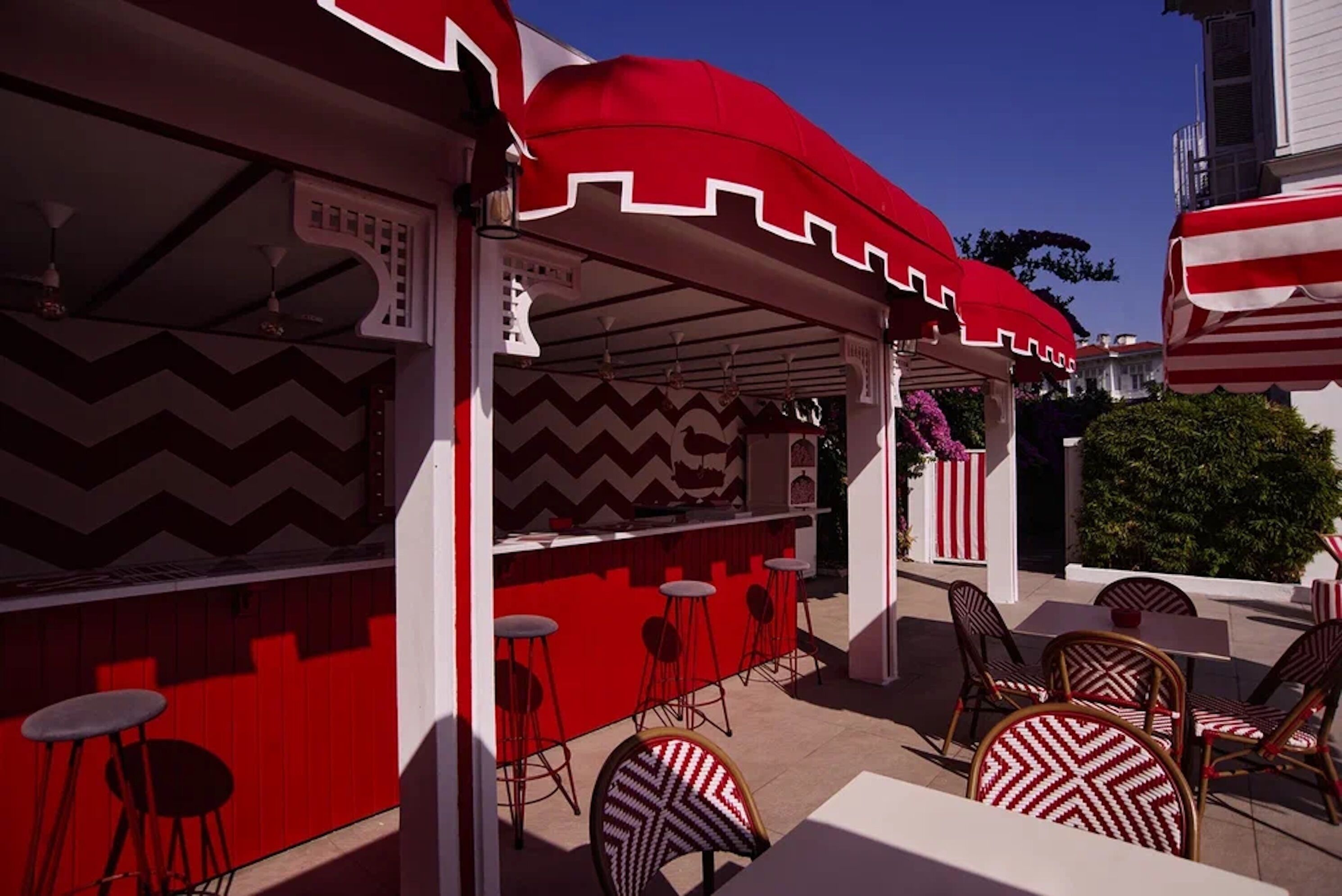 Een terras met rode en witte streepjes parasols, barstoelen en rieten stoelen.