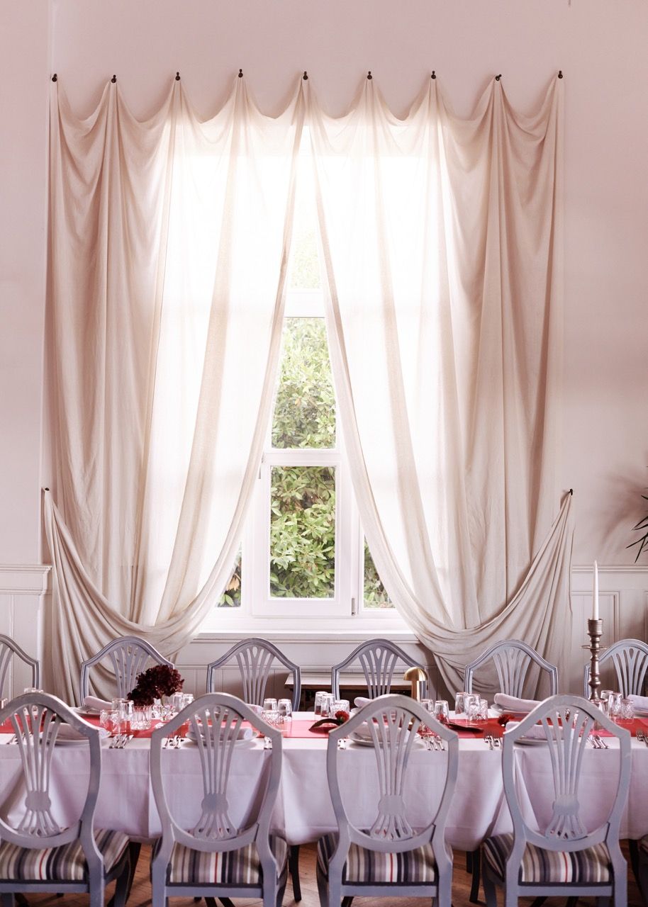 Una sala da pranzo con un tavolo imbandito per sei persone, tende bianche e una finestra che si affaccia sul verde.