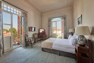 Habitación de hotel con una cama grande, un escritorio, dos sillas, un aparador y una ventana con vista a edificios.