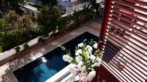 Un balcón con piscina, una mesa de comedor con un plato de comida y un jarrón de flores.