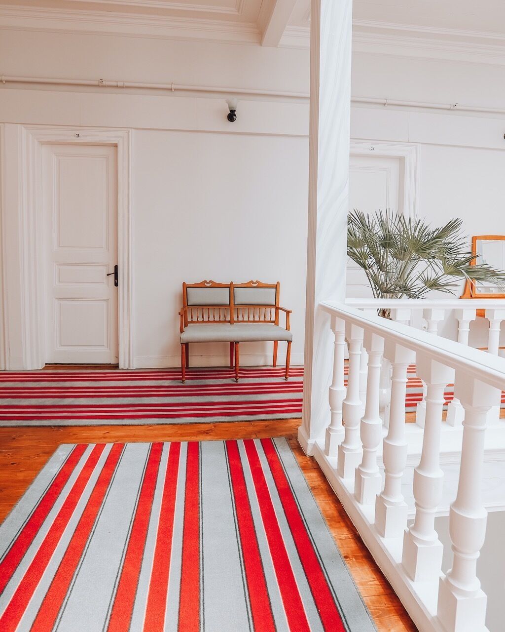 A hallway with a striped carpet, a wooden bench, and a white railing.