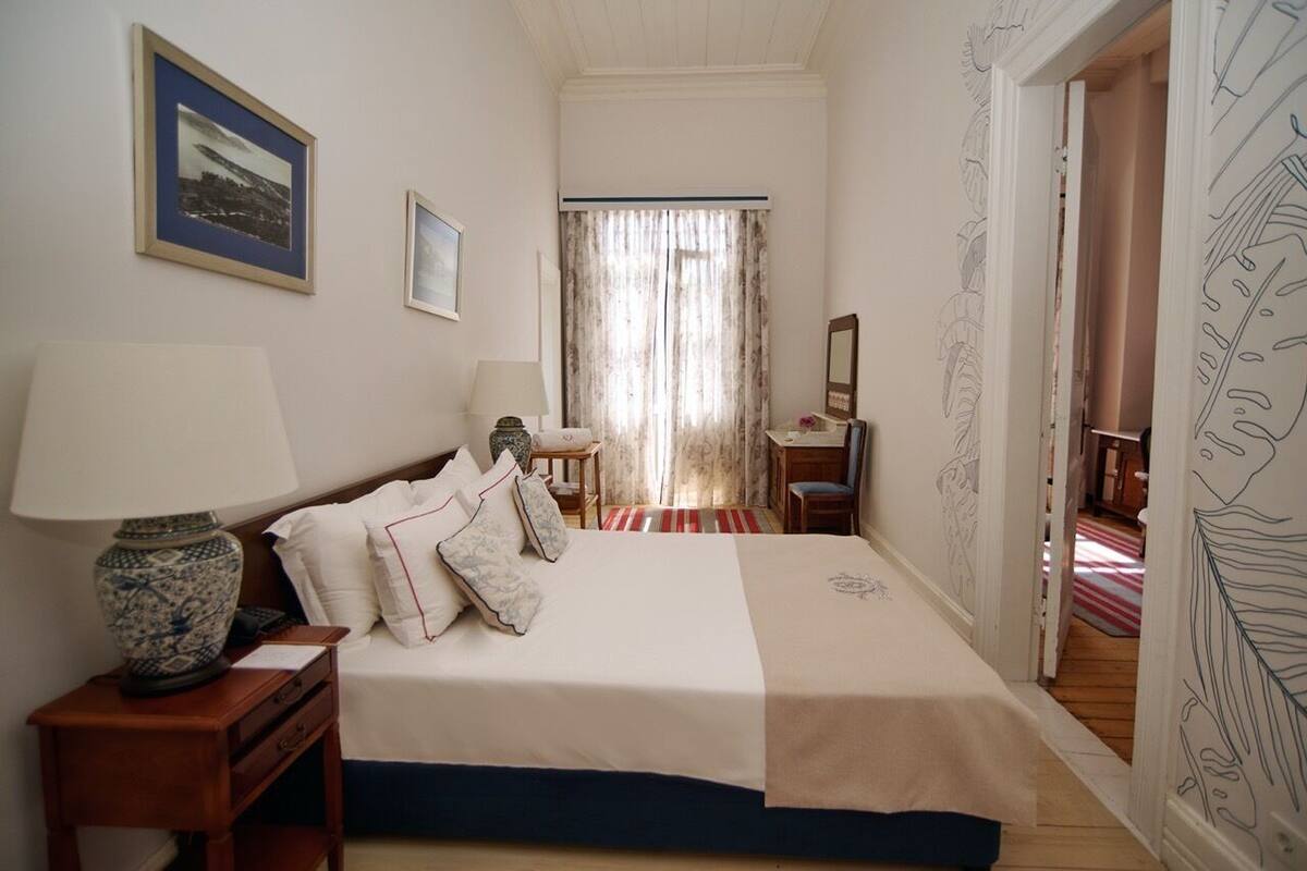 Une chambre à coucher comprenant un lit, une table de chevet, une lampe, une chaise, un bureau et une fenêtre avec des rideaux.