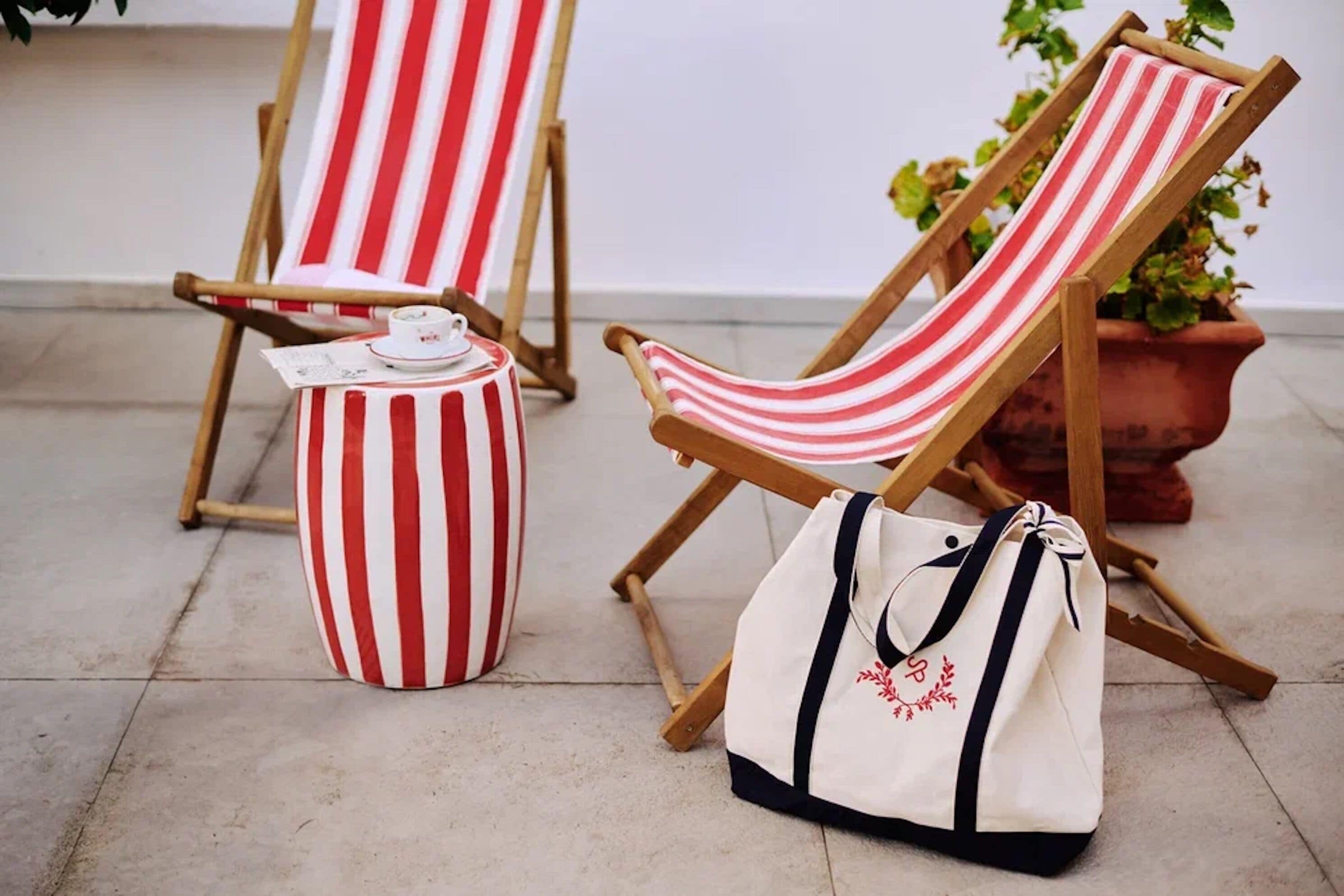 Una silla de playa a rayas, un taburete a rayas y un bolso de tela blanco con diseño floral.