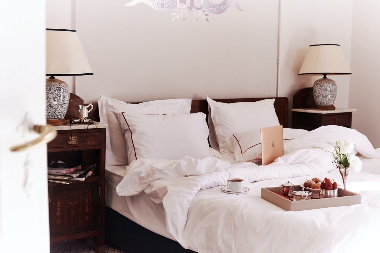 A neatly made bed with white linens, a laptop, and a tray with breakfast items.