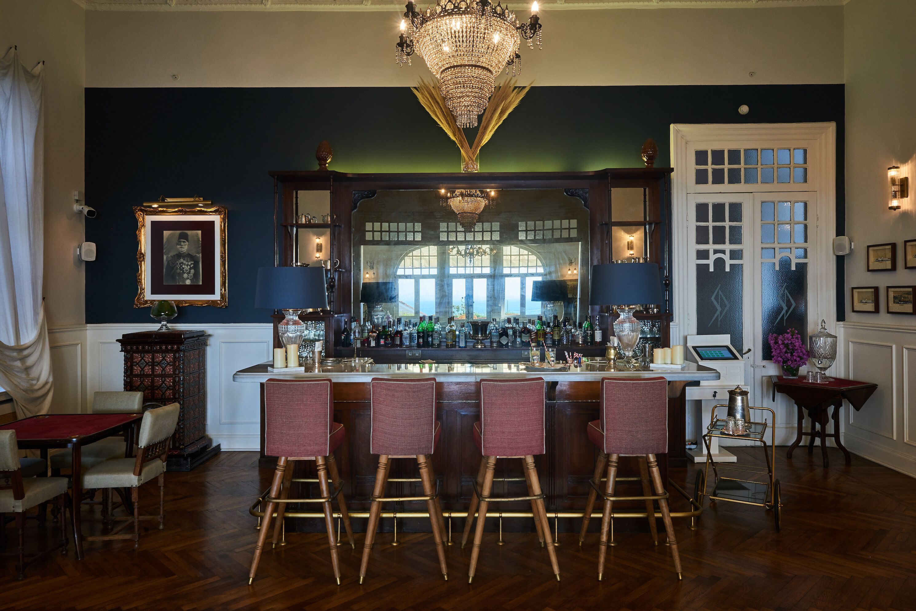 A bar area with a wooden bar counter, multiple stools, and a chandelier.