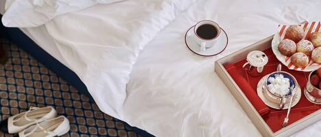 A neatly made bed with a pair of shoes, a cup of coffee, and a tray with pastries.
