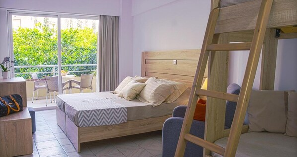 Un dormitorio con cama, escritorio, silla y balcón con vistas a la vegetación, además de una escalera de madera.