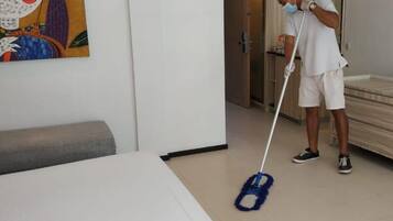 A person mopping a room with a white bed and a colorful painting on the wall.