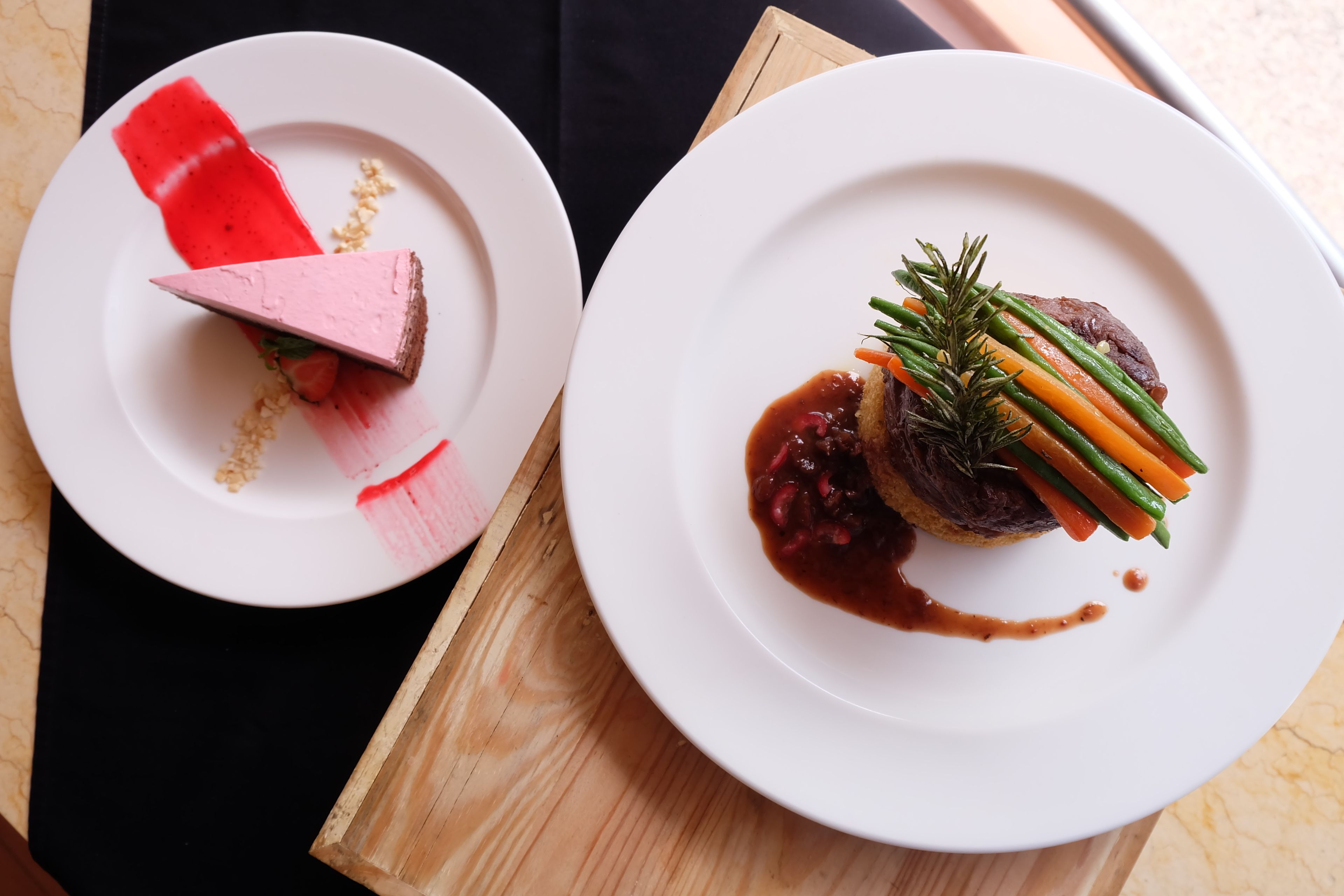 Two white plates with food on a wooden board.