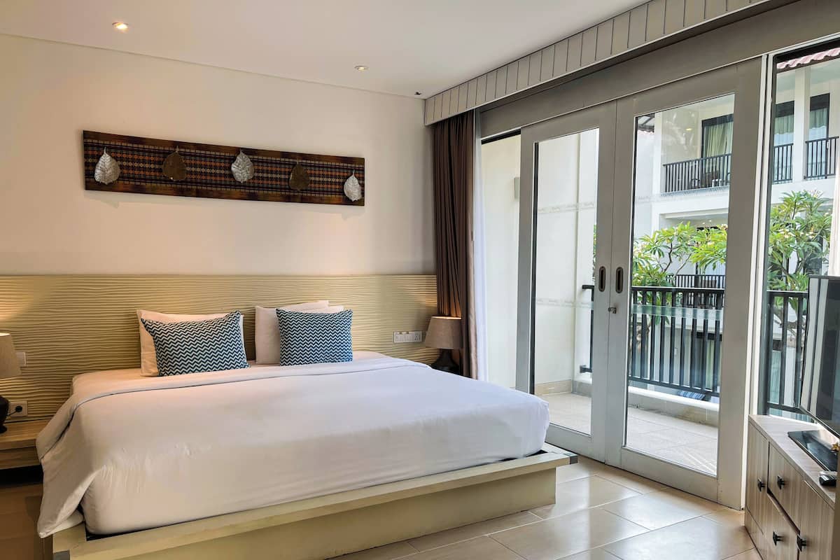 A modern hotel room with a large bed, a view of the outside balcony, and a decorative wall piece above the bed.