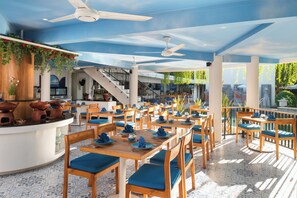 Un restaurante con varias mesas y sillas, una zona de barra y ventiladores de techo.