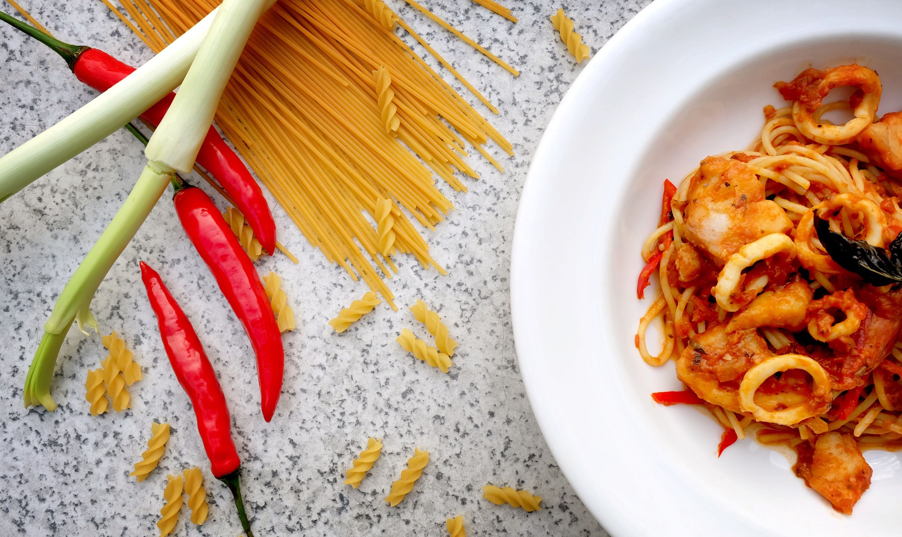 Un piatto di spaghetti con salsa di pomodoro e frutti di mare, pasta e peperoncino rosso su una superficie di marmo.