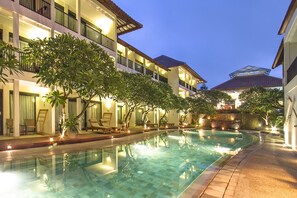 Un hotel con piscina, mobiliario exterior y una fachada bien iluminada.