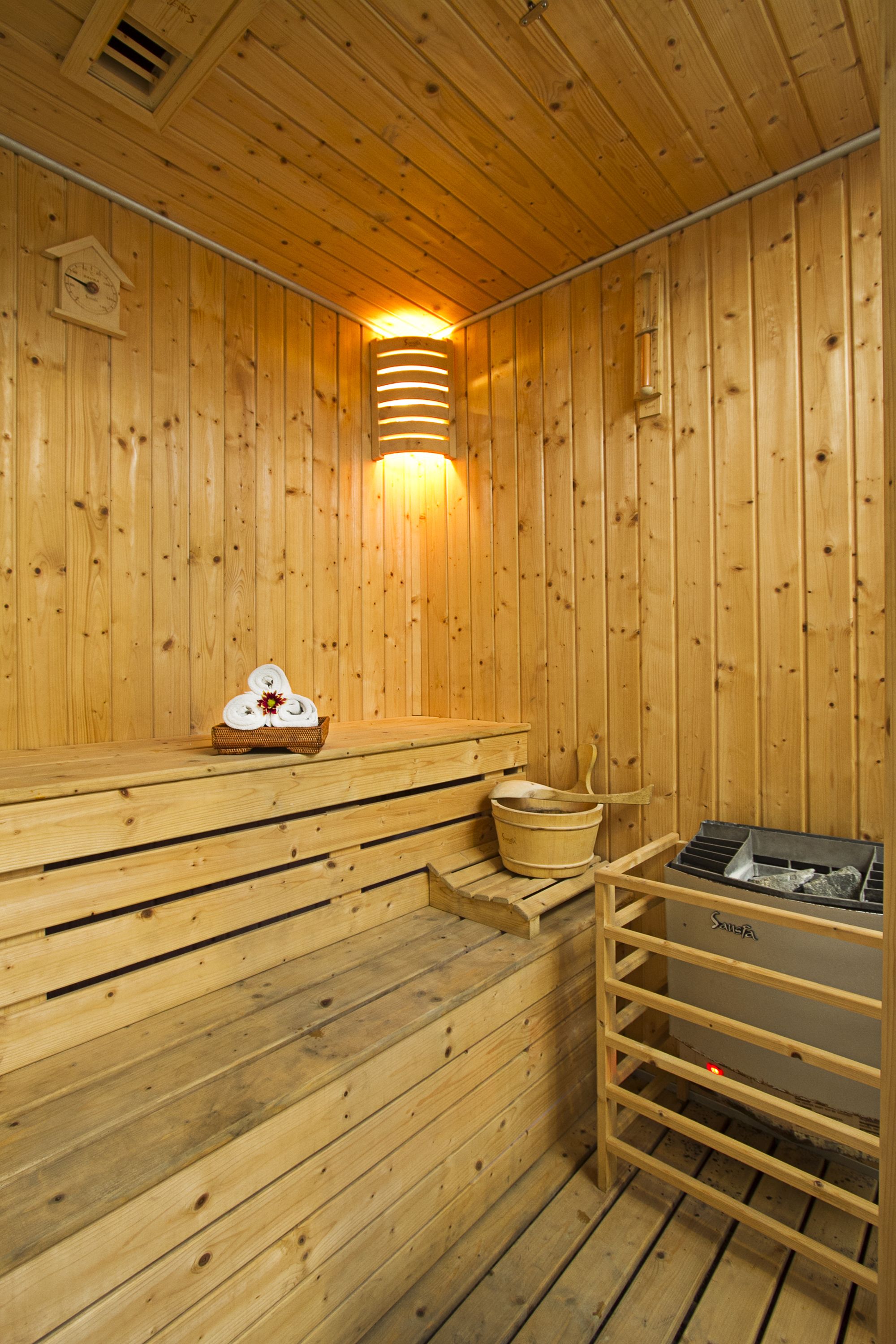 A wooden sauna with benches, a wall-mounted heater, and a sauna table with towels.